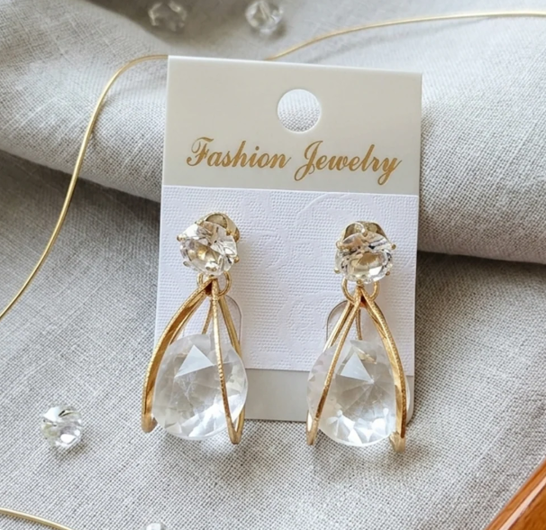 Crystal Teardrop Claw Earrings in Gold. A large clear teardrop crystal wrapped in sleek curved prongs, topped with a solitaire stud.