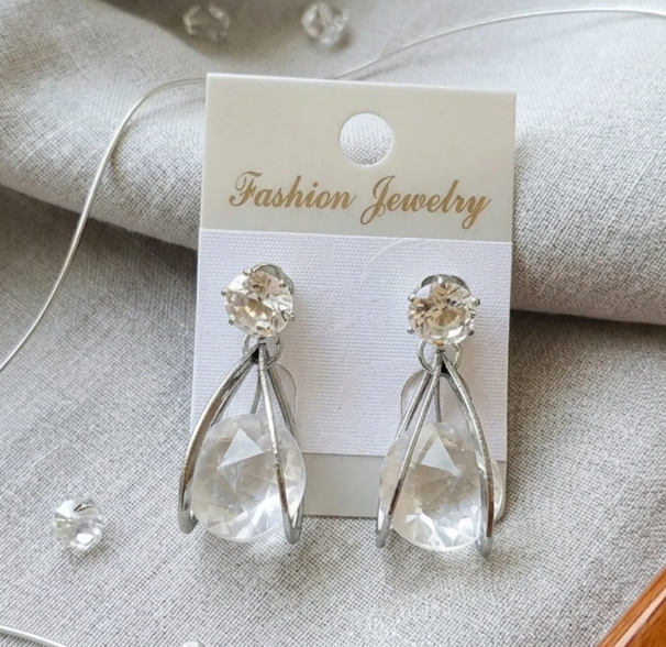 Crystal Teardrop Claw Earrings in Silver. A large clear teardrop crystal wrapped in sleek curved prongs, topped with a solitaire stud.